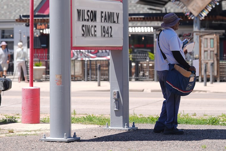 A U.S. Postal Service mail carrier keeps cool by standing in the shade of a gasoline station sign posting the per-gallon prices Thursday, June 4, 2026, in central Denver.