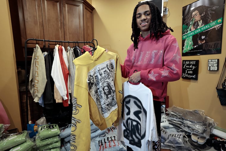Gavin Pennington, a senior at St. Joe's Prep, displays The Illest Club's "blessed" hoodie (left) and emoji tee (right) in their eadquarters based in his Voorhees home on Wednesday, March 6, 2025. The St. Joes Prep senior created the upscale streetwear line just a year and a half ago, and it has taken off.