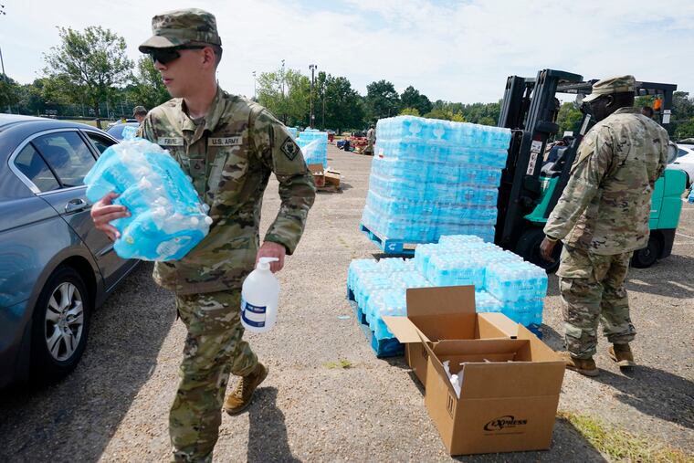 Mississippi National Guardsmen carry cases of drinking water and a bottle of hand sanitizer to Jackson, Miss., residents, Friday, Sept. 2, 2022, at Smith Wills Stadium. Jackson's water system partially failed following flooding and heavy rainfall that exacerbated longstanding problems in one of two water-treatment plants, and the state is helping with the distribution of drinking water to the city's residents. (AP Photo/Rogelio V. Solis)