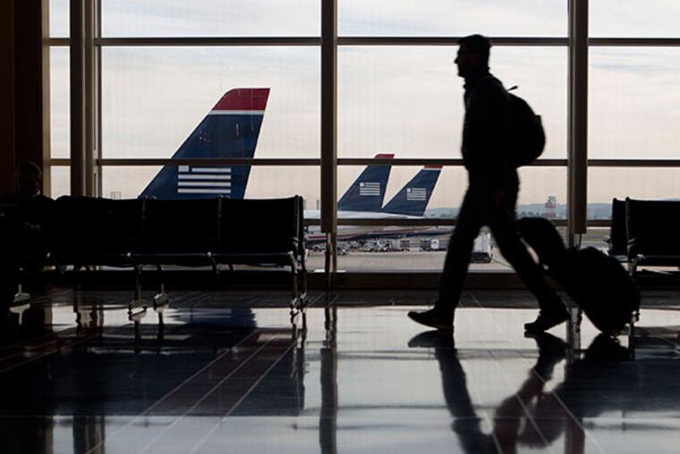 The silhouette of a traveler is seen walking past US Airways Group Inc. planes parked on the tarmac at Ronald Reagan National Airport in Washington, D.C., U.S., on Friday, Nov. 15, 2013. The U.S. settlement allowing the merger of American Airlines parent AMR Corp. and US Airways Group Inc. to go through will open the door to more low-cost carriers at Washington's Ronald Reagan National Airport. (Andrew Harrer/Bloomberg)