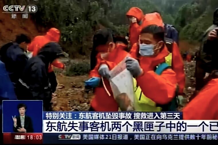 In this image taken from video footage run by China's CCTV, an emergency worker puts an orange-colored "black box" recorder into a plastic bag at the China Eastern flight crash site Wednesday.