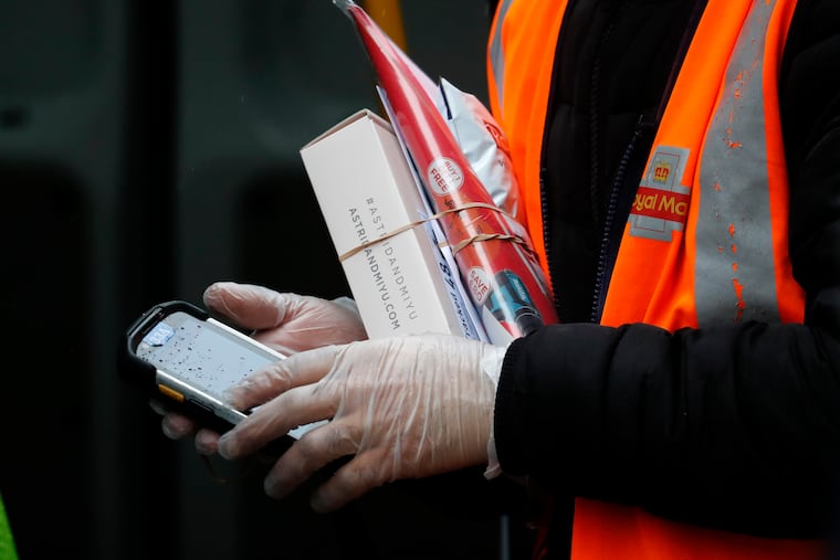 A Royal Mail employee wears gloves as he hold parcels and the signature handheld as he delivers in London.