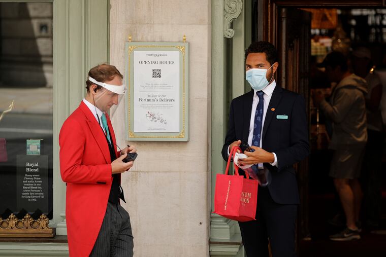 A doorman wearing a face shield to protect from coronavirus stands with a colleague at the main entrance of the Fortnum & Mason department store in the Piccadilly area of central London.