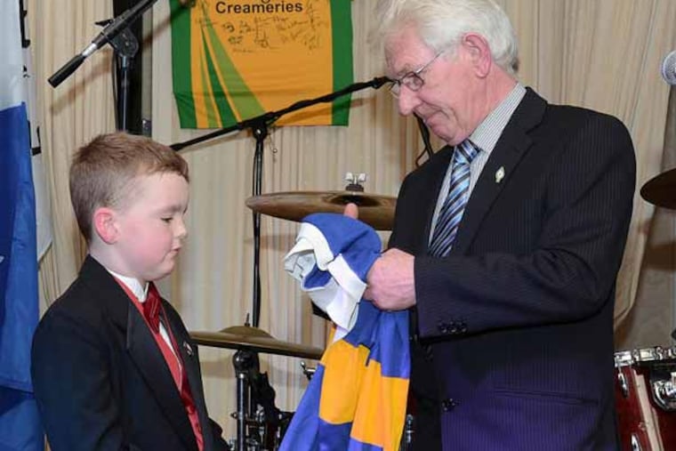 Sean Dunlop, Charlie Dunlop's father, (right) presents a football jersey to his grandson, little Charlie, (left) Charlie Dunlop's son. The jersey, a replica of one that Charlie Dunlop wore when he played for a team in Ireland, was made by the team to honor their former teammate. (Photo courtesy of Denise Foley, irishphiladelphia.com)