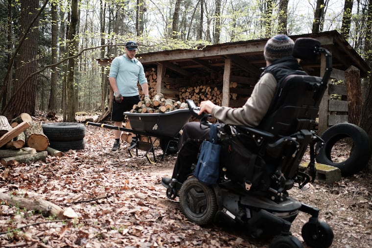 Army veteran Adam Perry loads and stacks firewood while Todd Gladfelter looks on from his motorized wheelchair, in New Ringgold, Pa., on April 28, 2024.