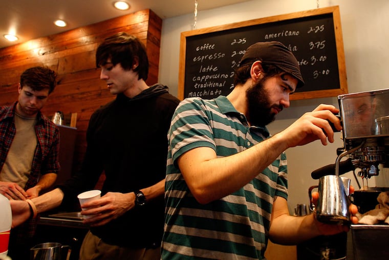 Charlie Biando (right) keeps his eye on the espresso as he steams a pitcher of milk for a cappuccino, as Elixr owner Evan Inatome (center) and manager Brian Honsinger work the counter at their Philadelphia coffee shop in 2018.