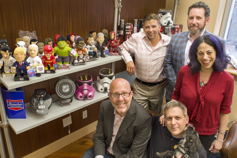 Bleacher Creatures’ founder Matthew Hoffman (left, front) and Pangea Brands CEO Ed Strauss (right, front, holding dog Minnie) and associates in New York on Sept. 28. Behind them, from left, are Jeremy Kelley, Jason Davidman, and Peggy Strauss. The two companies — whose products are featured on the shelves — have combined to become Uncanny Brands.