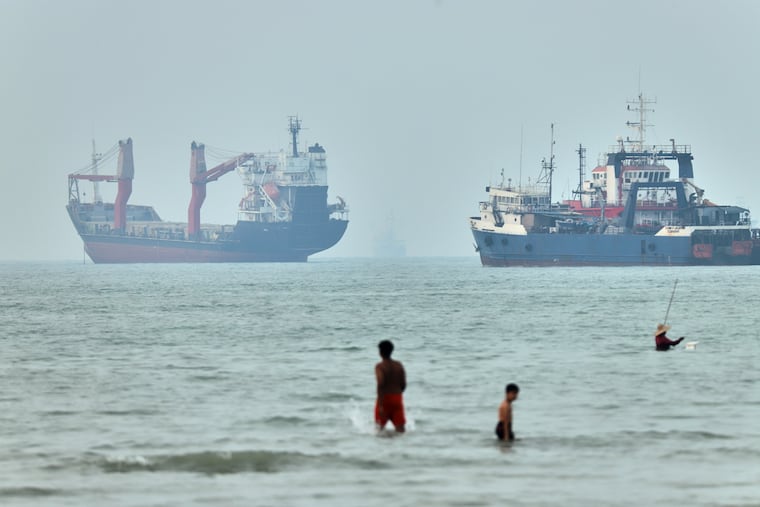 Children wade in the water with cargo ships at anchor in the background and a fisherman nearby, in the Strait of Hormuz off Bandar Abbas, Iran, Tuesday, June 30, 2026.