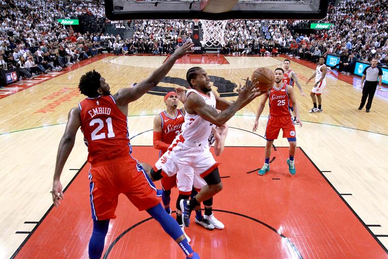 Kawhi Leonard (center) goes up and under for layup against Joel Embiid on Sunday.