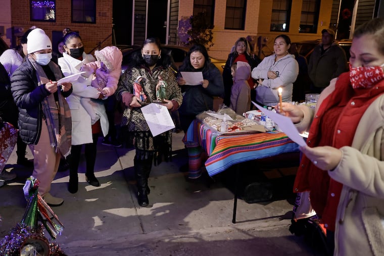 Mayra Rufino (centro) presenta las estatuas de José y María mientras Olivia Rodríguez (derecha) y otras miembros del Mercado de Latinas cantan villancicos durante una posada en la casa de Reyna Guadalupe Navarro en el sur de Filadelfia, el 17 de diciembre de 2021.