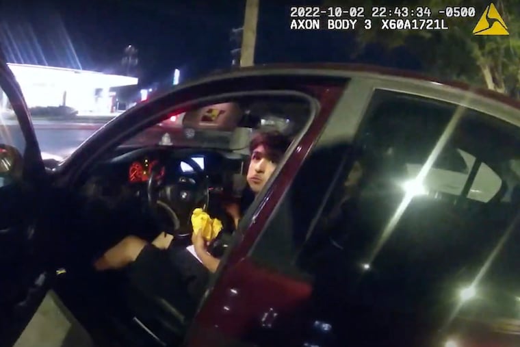 In this image taken from Oct. 2, 2022 police body camera video and released by San Antonio Police Department, Erik Cantu looks toward San Antonio Police officer James Brennand while holding a hamburger in a fast food restaurant parking lot as the officer opens the car door in San Antonio, Texas.