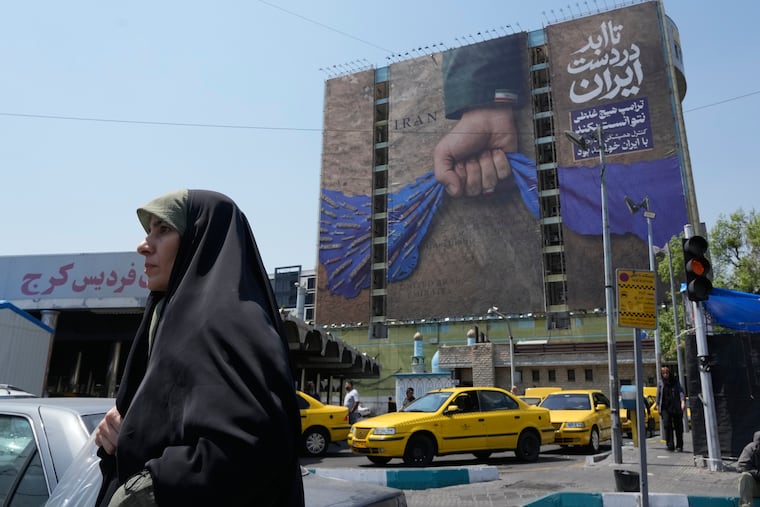 A woman walks past a billboard in Tehran, Iran Thursday that shows a graphic depicting a hand holding the Strait of Hormuz and anti-American slogans, including “The control of Strait of Hormuz will be Iran's forever.”