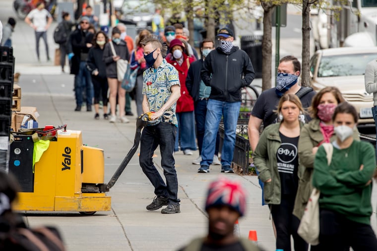 In this April 14, 2020 file photo, a Trader Joe's grocery store employee takes in food as the line to get in the store stretches down a city block on 14th Street and U Street in Washington. Moody's economist Mark Zandi says an economic recovery should begin by Memorial Day, but the economy won't fully recover for several years, assuming a vaccine is made and the Federal Reserve's safety net holds. (AP Photo/Andrew Harnik)