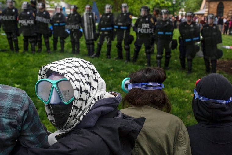 A pro-Palestinian demonstrator wears goggles and a mask as police with riot shields and protesters stand across from one another on the grounds of the University of Virginia, in Charlottesville, Va., in May 2024.