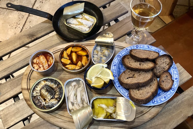 A tasting of tinned fish at Craig LaBan's house included, clockwise from top, a pan of warmed Brittany sardines in buttter and sea salt, Spanish cockles, cod poached in oil, Spanish razor clams, grilled sardines from Asturias, butter-poached lobster from Canada, and Spanish fried mussels in escabeche.