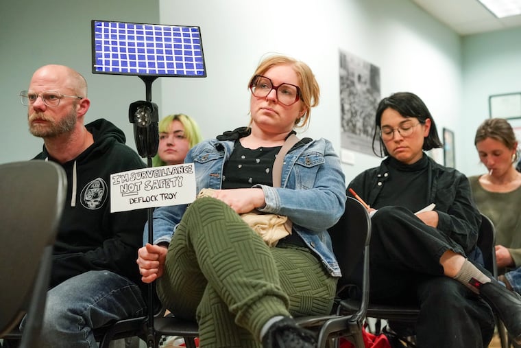Bri Harrington holds a sign and a handmade Flock camera prop during a council meeting in Troy, New York, in April.
