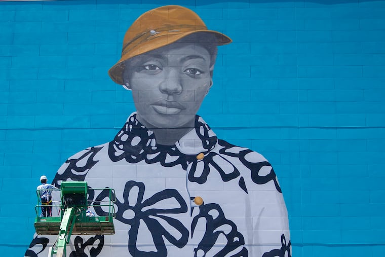 Arthur Haywood works to install a mural by Amy Sherald, the woman who painted the portrait of Michelle Obama for the Smithsonian, at 1109 Sansom in Center City Philadelphia on Wednesday, May 22, 2019. The girl in the mural, Najee Spencer-Young, is from North Philly.