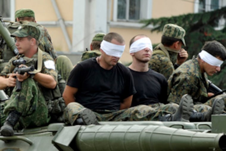 Bound and blindfolded Georgian soldiers sit atop an armored personnel carrier, held as Russian prisoners in Poti, Georgia. While some Russian troops began leaving Georgia, others seemed to be digging in. Meanwhile, NATO told Moscow that relations would suffer until all of its troops withdraw. Stories on A4.