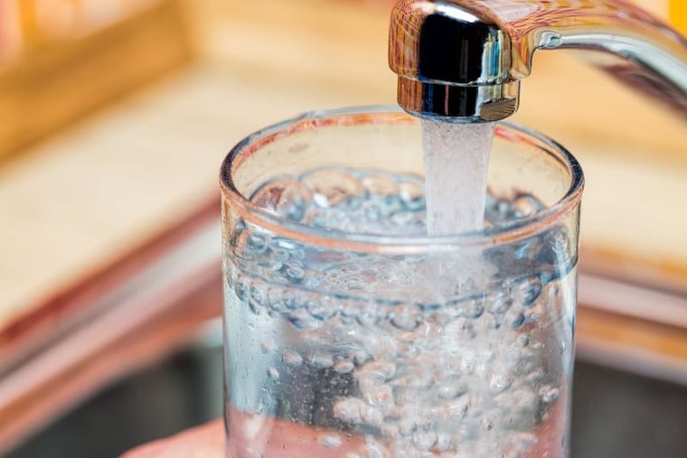 Water is pictured flowing into a glass from a kitchen faucet.