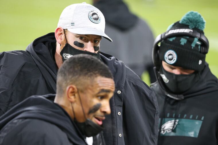 Eagles QB Carson Wentz (background) watches as Jalen Hurts talks with their teammates after Hurts threw a touchdown pass to Greg Ward in Sunday's 30-16 loss to the Packers.