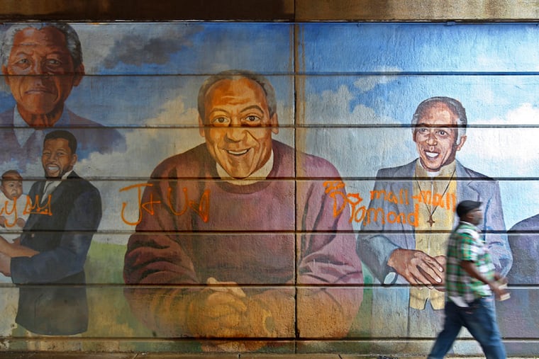 A portrait of Bill Cosby stares out at passersby as they walk under the bridge at North Broad Street near Indiana. The city's Mural Arts Program plans to remove a mural. ( Michael Bryant / Staff Photographer )