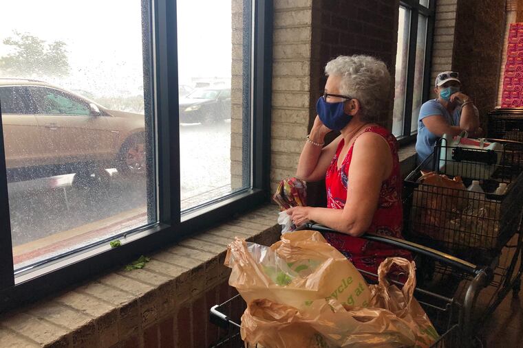 Grocery shoppers wait in the entrance at Wegman’s in Cherry Hill on Saturday for a powerful thunderstorm to pass before going to their cars. The storm knocked out power in the store, but backup generators kicked in.