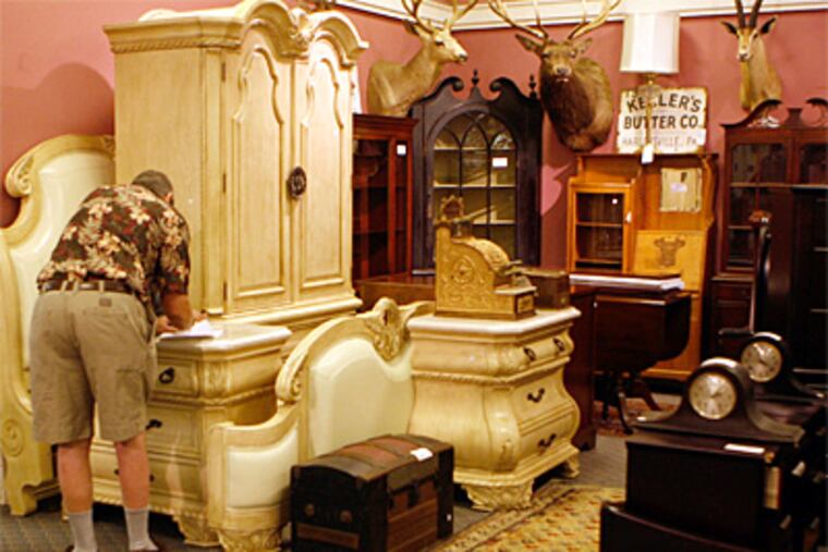 A prospective bidder examines furniture seized from the Montgomery County home at Alderfer Auction & Appraisal. (Bonnie Weller / Inquirer)