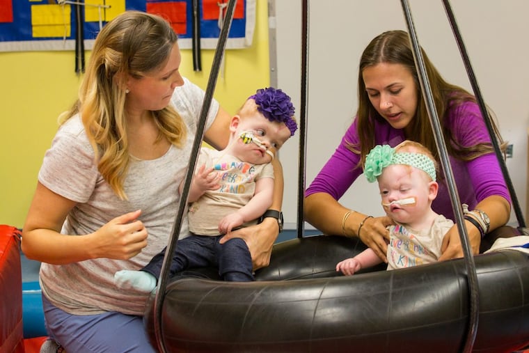Occupational therapist Ashley Binkowski (left) holds Abby Delaney, while therapist Anne Borema supports her twin Erin, during a session at CHOP.