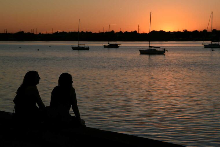 Mackenzie Cunningham (left) and Sarah O'Connor, both 22, from Cinaminson watch from Riverton, NJ, as the sun sets over the Delaware River as the summer solstice ends June 21, 2017.