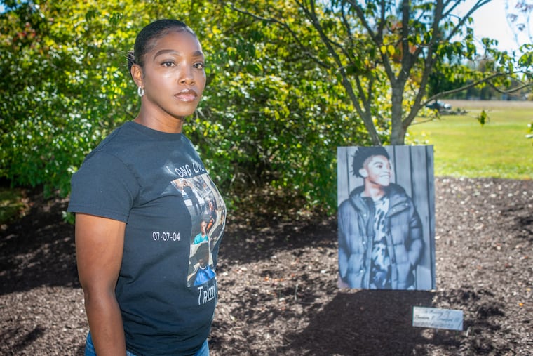 Cherisse Pearson stands near a portrait of her son, Theodore "Trae" Crawford, near a tree planted his memory. Crawford was shot and killed in 2022, and his killing is one of many solved this year.