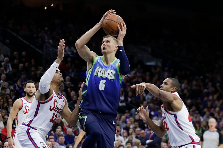 Dallas Mavericks forward Kristaps Porzingis drives to the basket against Sixers forward Tobias Harris and center Al Horford on Friday, December 20, 2019 in Philadelphia.