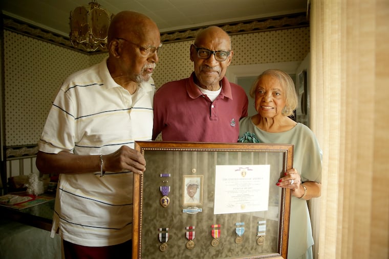 Harry Robinson, 86, left, Wallace Robinson, 81, and Mary Robinson, 84, right, hold up a tribute to their brother Joseph Robinson in Elkins Park, PA on June 18, 2018. Cpl. Joseph Robinson died a prisoner of war in North Korea in 1951.