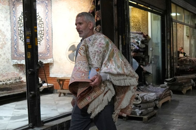 A man carries a carpet in hand-woven carpets market at Tehran's traditional main bazaar, Iran, Saturday, Aug. 8, 2026.