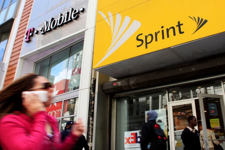 A woman using a cell phone walks past T-Mobile and Sprint stores in New York.