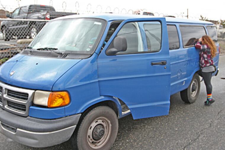 Azean Malik, the band's manager, stands on tiptoe to check that everything is still in the band's van after it spent the night in the PPA Impound lot in South Philadelphia. (Michael Bryant/Staff)