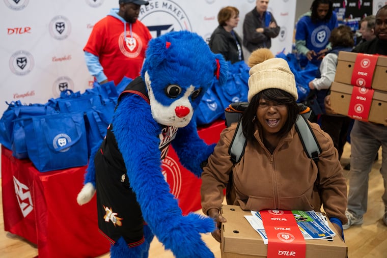 Kathleen Pointer is greeted by Sixers mascot Franklin as the Tyrese Maxey Foundation provides Thanksgiving meals on Saturday.