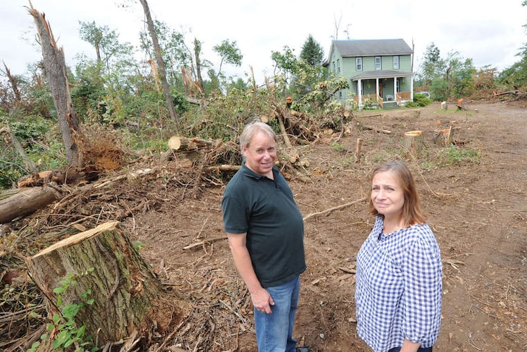 Rob and Pam Kafka stand amid trees downed by a June 23 storm that devastated Clarksboro and other parts of Gloucester County. In the background is the home of their daughter Molly.
