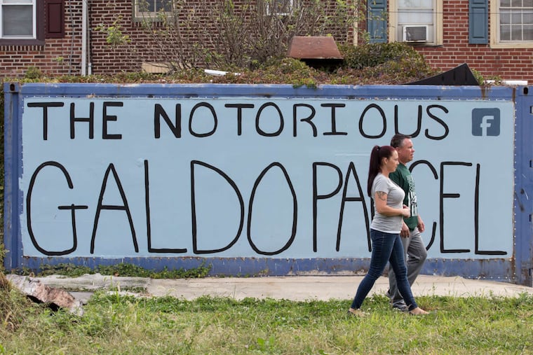 Frank Galdo, back, and his wife Nicole Galdo, front, shown here on the vacant lot across the street from their house, Frank has been maintaining and improving the lot for over twenty years, in Fishtown, Wednesday, Oct. 11, 2017. The couple are walking in front of a large sign publicizing their plight. Galdo paved a driveway, built a fire pit and a treehouse, but the city wants the land back. Galdo lost the first round in court, and is pursuing an appeal using an "adverse possession" legal argument. JESSICA GRIFFIN / Staff Photographer