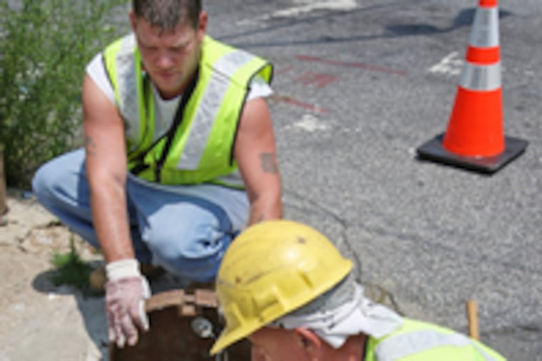 City Water Department workers Fred Feoli (left) and John Mock installed a chain yesterday to secure an inlet cover at Tulip and Somerset Streets.