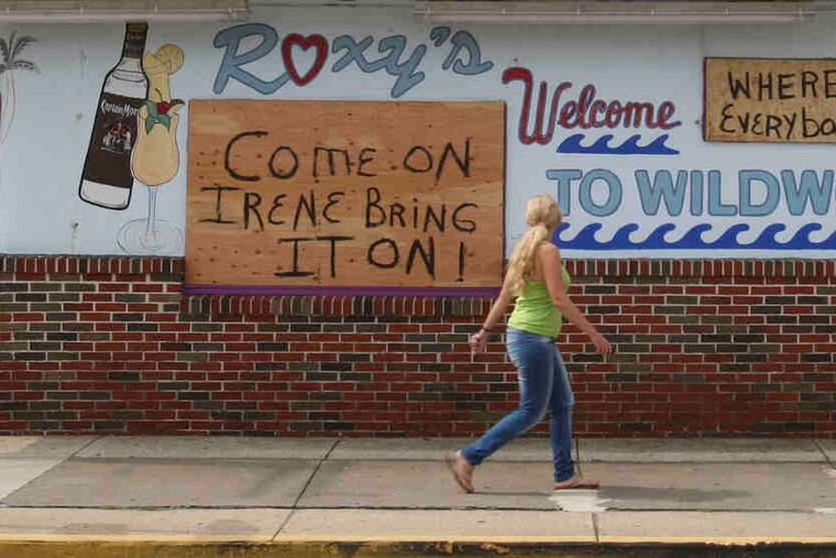 Julia Gorbava from Russia walks past signs on a boarded-up business in Wildwood. Roads usually clogged with inbound traffic on a summer afternoon were jammed Friday with motorists evacuating the Shore, and beaches were mostly deserted.