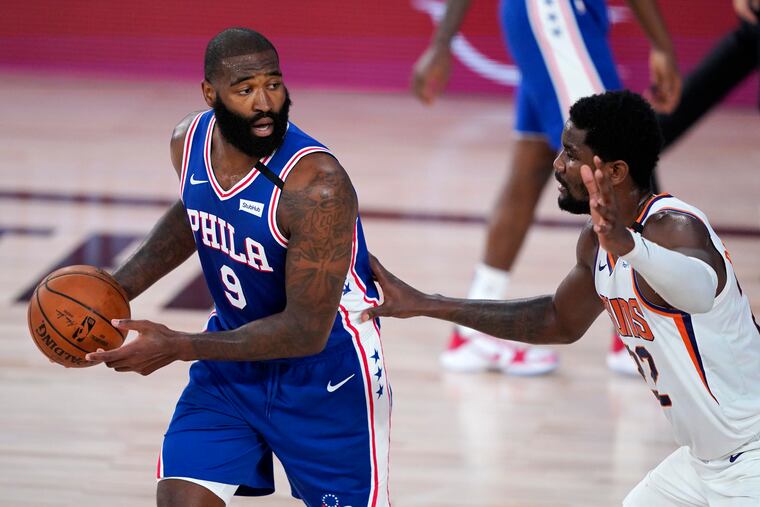 Sixers center Kyle O'Quinn looks to make a pass while guarded by Suns center Deandre Ayton.