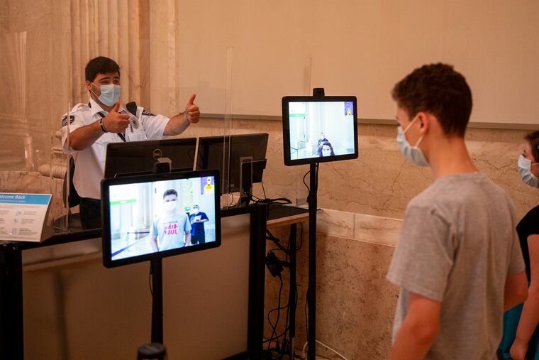 Matthew Mackara, 23, of South Philadelphia, gives a thumbs up to visitors after checking their temperature at the Franklin Institute on Wednesday, July 8, 2020. The museum has had significant safety measures in place such as hand sanitizer stations and disinfecting wipes, plexiglass barriers and marked spots for social distancing.