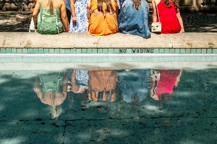 June 2, 2025: Summer sundresses on a spring Saturday in the Square. Friends meet and are reflected in the water of the Rittenhouse Square fountain.