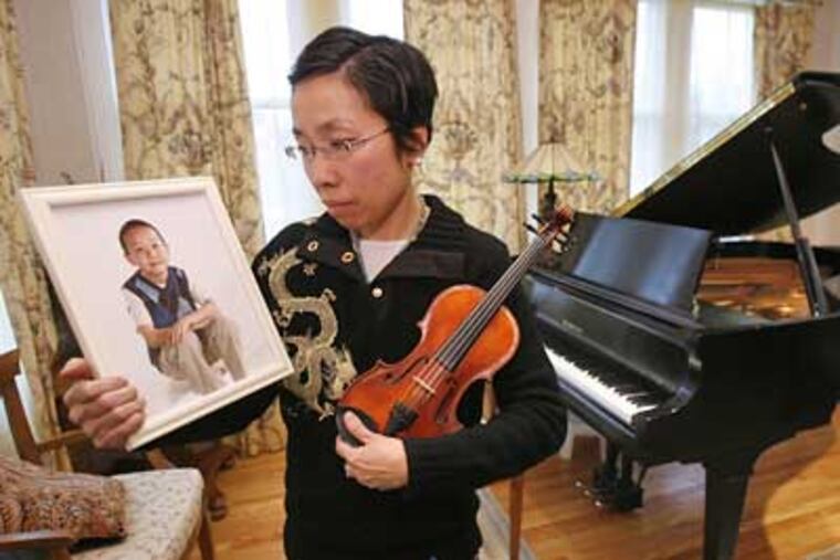 Catherine Lee holds a photo of her son, Chanlan Lee, and his violin. Chanlan Lee was a standout violinist at the Nelly Berman Music School before his death at age 8. (Charles Fox / Staff Photographer)