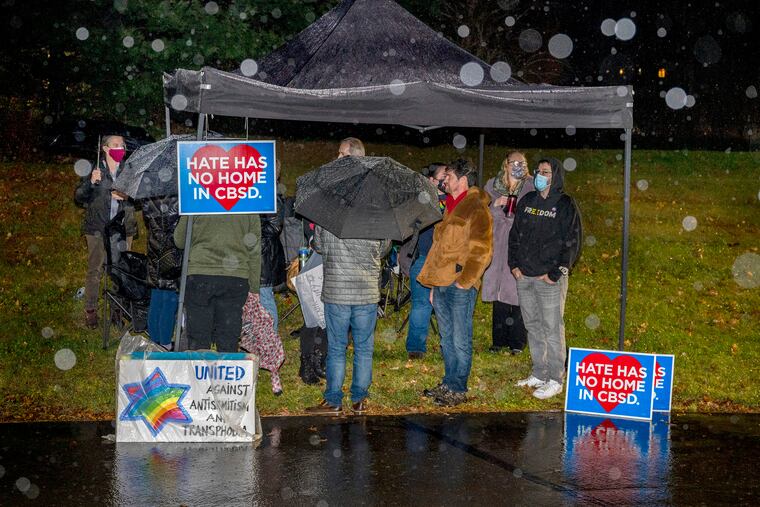 Community members wait in the rain with their signs outside the Central Bucks School Board meeting on Dec. 6. The district announced schools would be closed Monday due to an unprecedented number of teacher absences because of a surge in COVID-19 cases.
