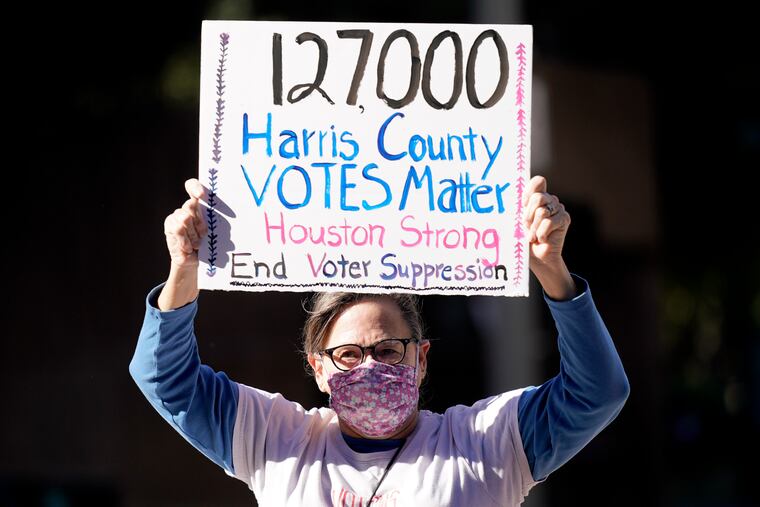 Demonstrator Gina Dusterhoft holds up a sign as she walks to join others standing across the street from the federal courthouse in Houston, before a hearing in federal court involving drive-thru ballots cast in Harris County.