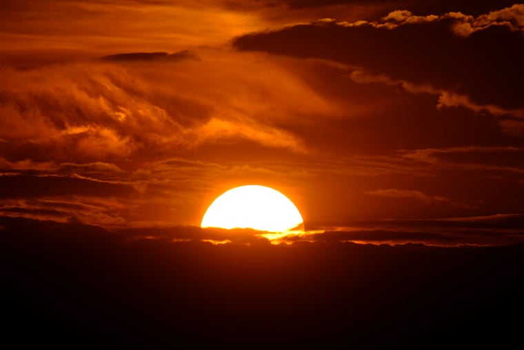 The setting sun illuminates the clouds over the Rocky Mountains after a third straight day of record-breaking heat Sunday in Denver.