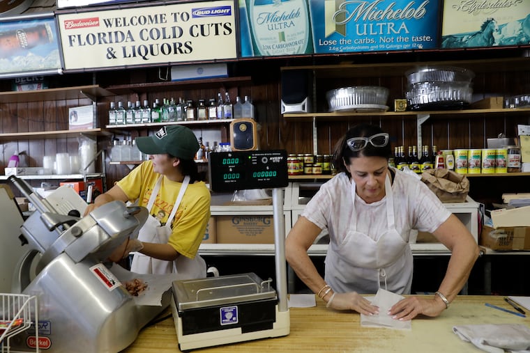 Tiffany Rando (left) slices baked ham while mother-n-law Lisa Borrelli folds the sliced ham in wax paper behind the counter at the Florida Cold Cuts & Liquors in Ventnor City, New Jersey on Friday, June 24, 2022.