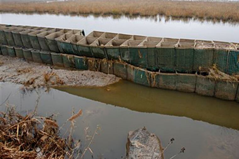 In this Dec. 8, 2012 photo, the battered and emptied Richard P. Kane Wetland Mitigation Bank, a long barrier wall made of large baskets filled with sand and dirt, runs through the Meadowlands in Moonachie, N.J. The barrier was built primarily to control the movement of tidewaters in and out of the wetlands area and not for flood protection. But since the tidal surge from Superstorm Sandy washed over it and damaged more than 2,000 homes and other buildings, attention has turned to what can be done to prevent similar river flooding in future storms. Unfortunately, however, no one seems to own the problem. (AP Photo/Mel Evans)