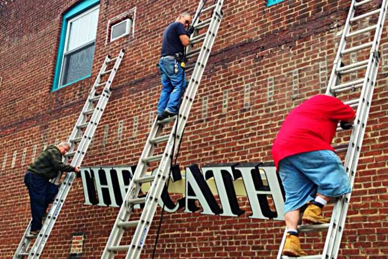 From left, workers from Bernard Sign, Larry Szymkowiak, Rainman Snow and John McElroy take down the Catholic Shop sign from the side of the building where the shop is, on York Rd. in Willow Grove. (Photo by Carolyn Davis)